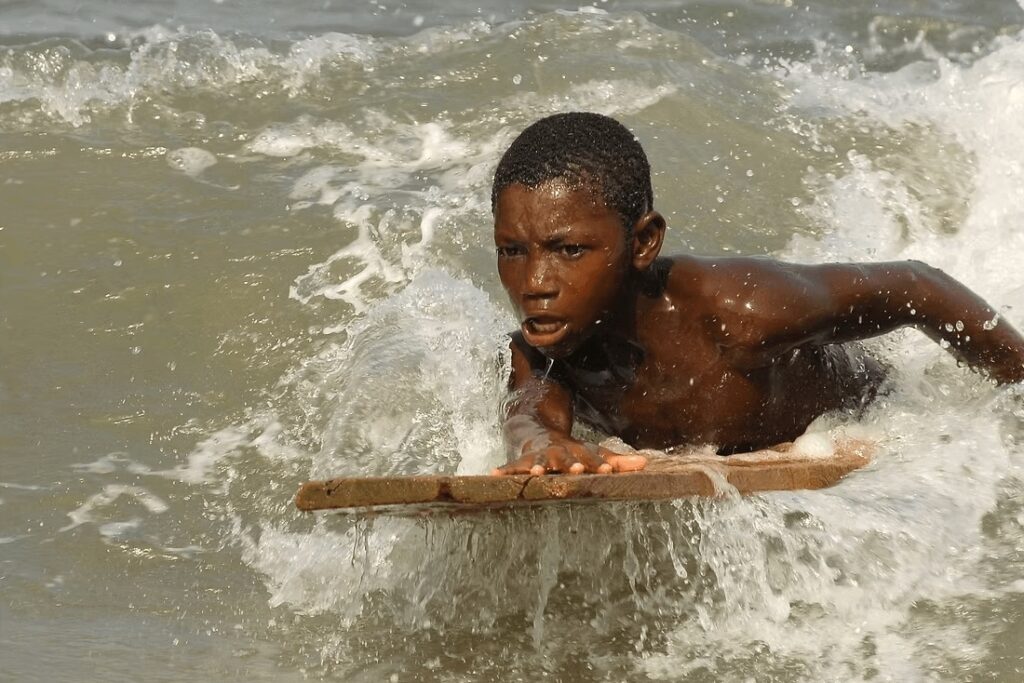 Best Ghana surf spots: A young Ghanaian boy riding a wooden surfboard