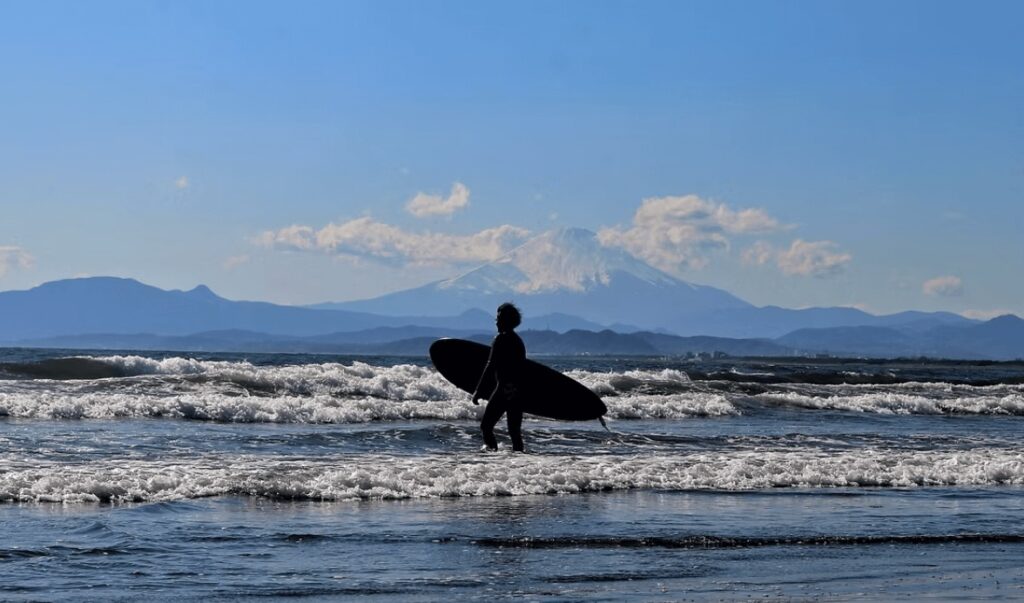 Best surf spots in Japan: A silhouette of a surfer against a snow-capped volcano in Japan