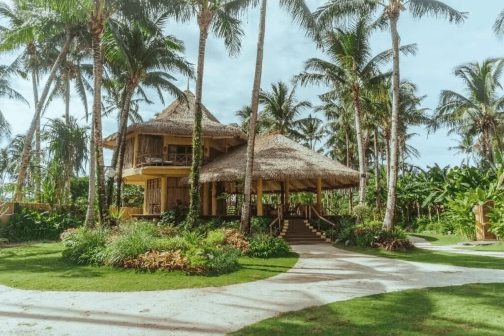 Sustainable resorts in Siargao, PhilippinesThatched-roof buildings surrounded by palm trees at Inara, one of the best eco-hotels in Siargao