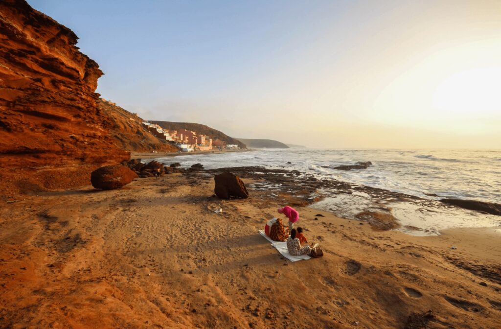 Best surf spots in Morocco: Local women watch sunset backed by the ochre cliffs of Mirleft