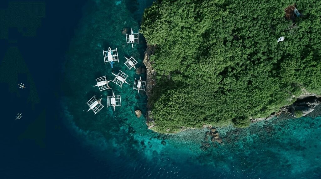 A bird's eye view of outrigger boats along a rocky coastline in the Philippines