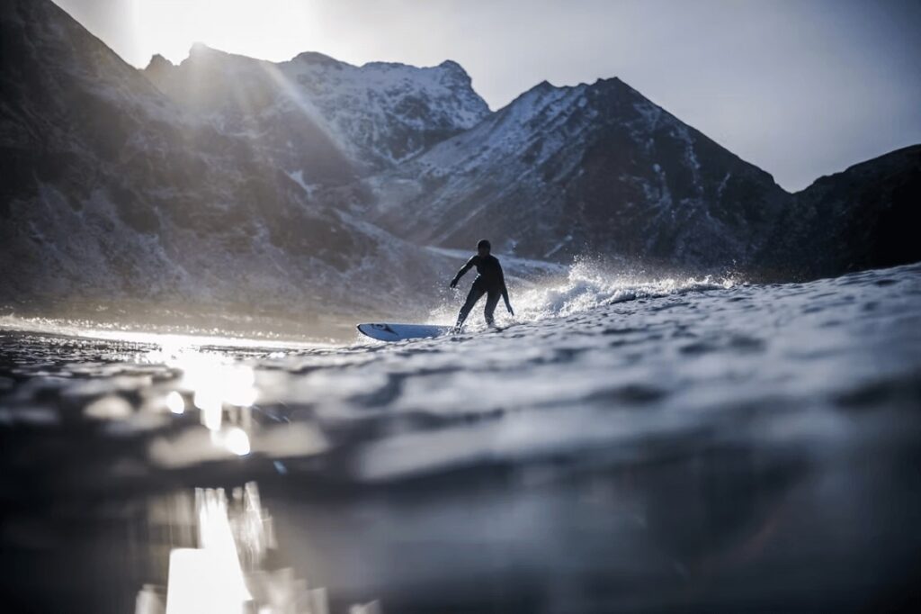 A surfer braving the icy waters in front of Unstad Arctic in the Lofoten Islands 