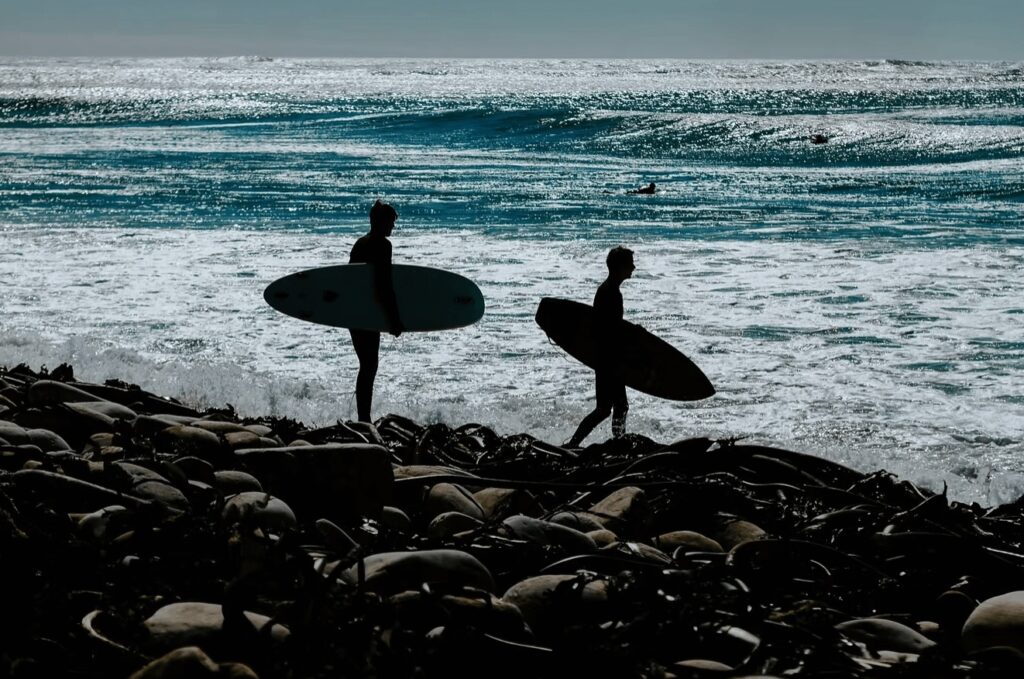 A silhouette of two surfers entering the water along a rocky coastline