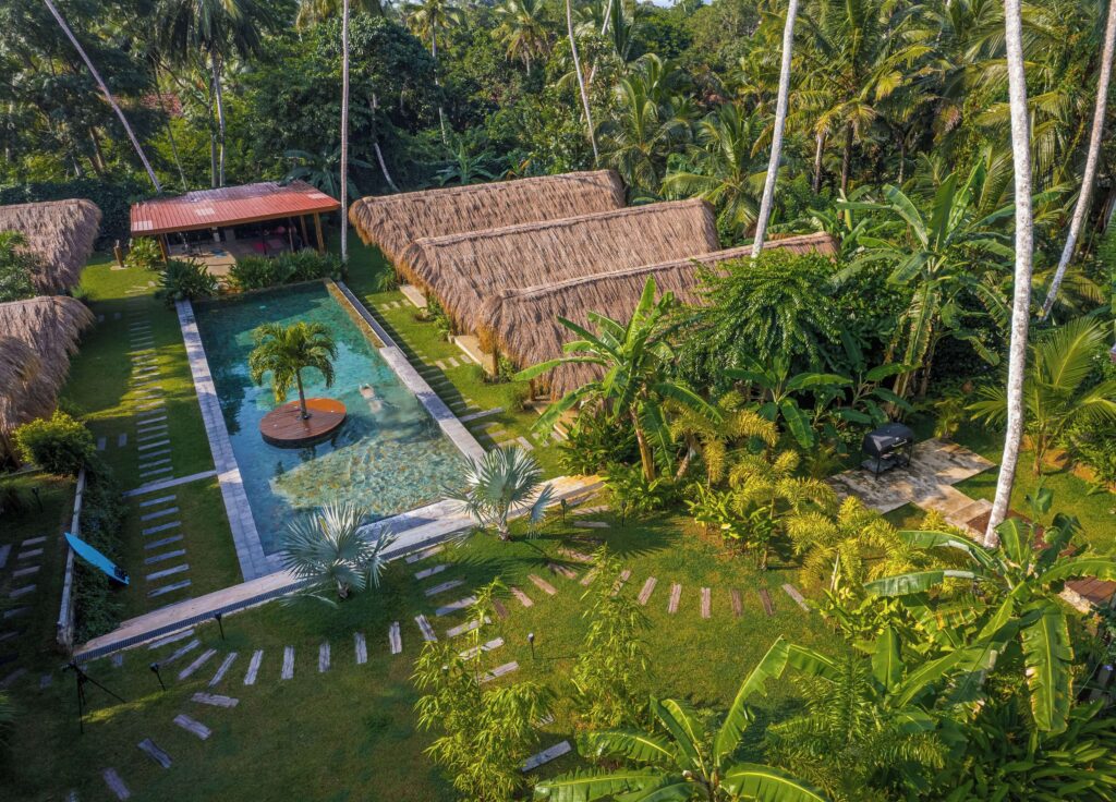 An elevated view of the swimming pool and thatched roof bungalows of The Jungalows