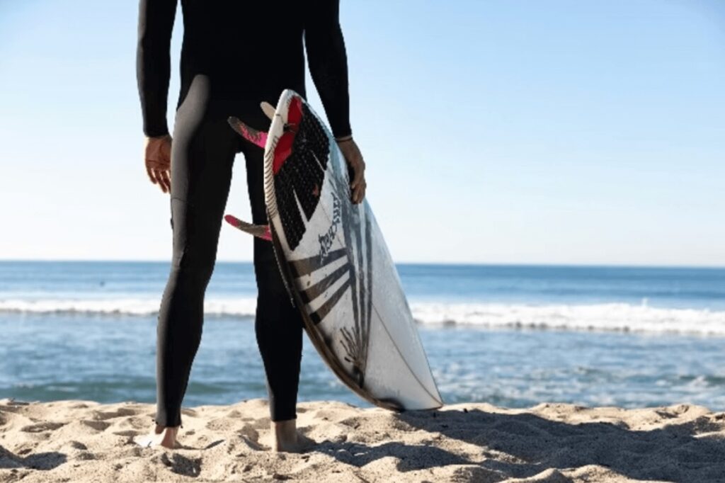 A surfer on a sandy beach looks out toward the waves