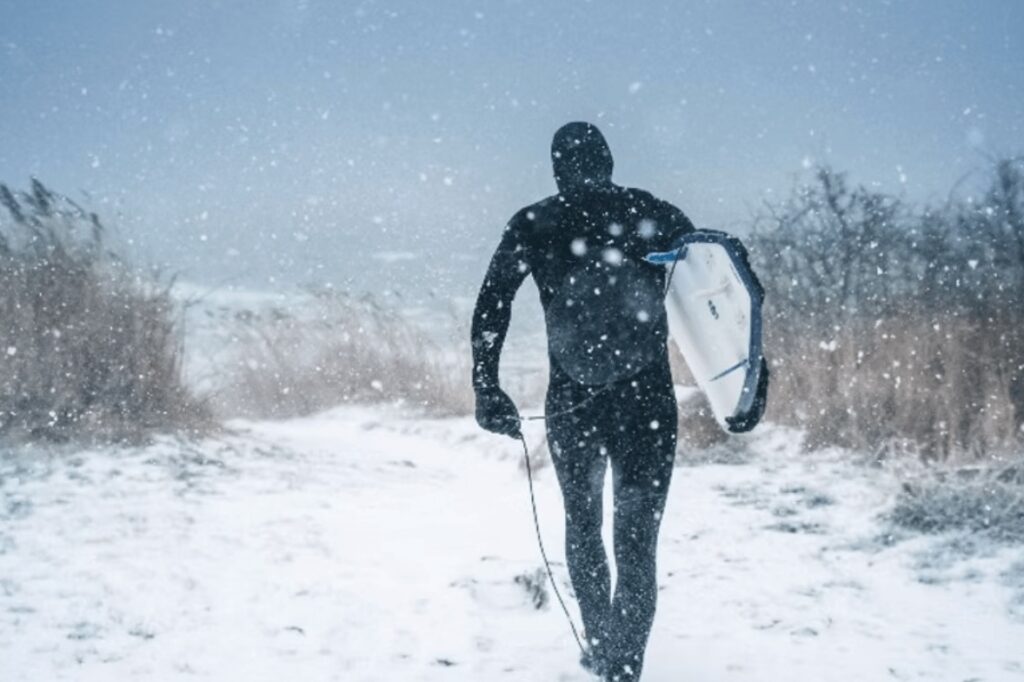 The environmental impacts of neoprene wetsuits: A surfer walking through the snow with a board