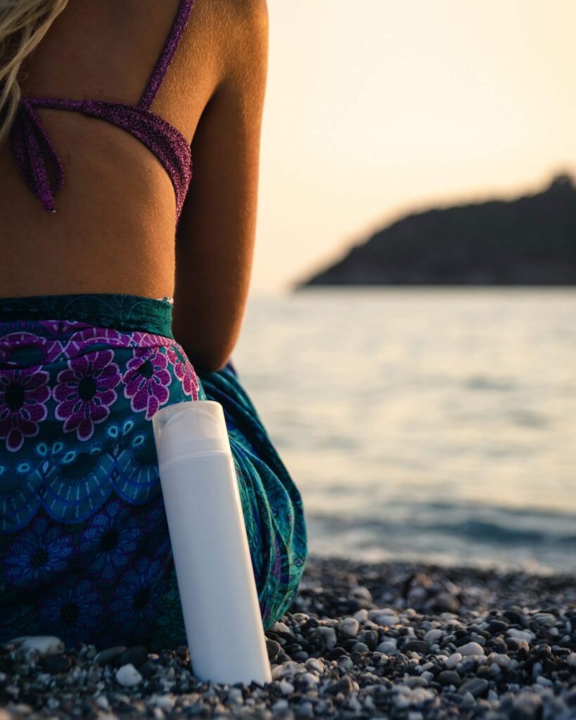 Sunscreen in a tube beside a woman sitting on a beach