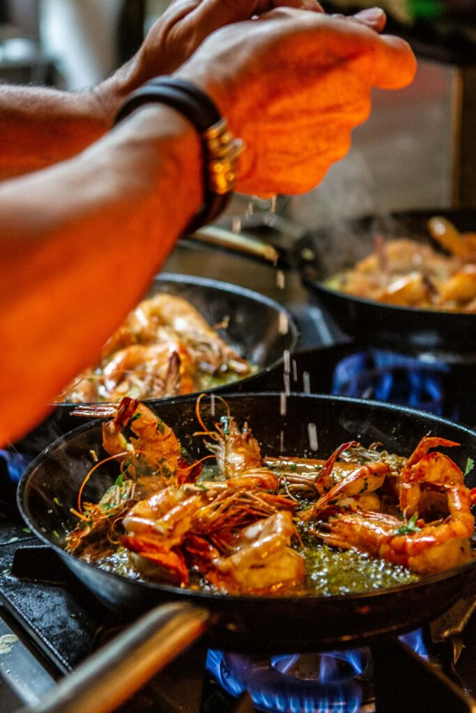 A chef squeezes a lemon into a pan of prawns
