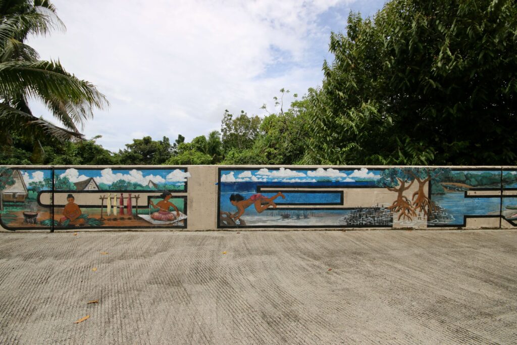 A mural depicting traditional Palauan scenes on the side of the road
